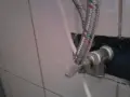 Metalowy króciec z zaworem, do którego podłączony jest elastyczny przewód w oplocie.
