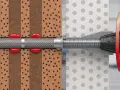 Przekrój przez materiał budowlany pokazujący działanie kotew chemicznych. Czerwona żywica wypełnia otwory w materiale, tworząc mocne połączenie.