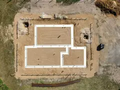 Widok z lotu ptaka na budowę domu. Widoczne są różne rodzaje fundamentów, w tym ławy fundamentowe i wykopy pod słupy.
